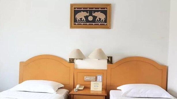 A hotel room with two single beds, a wooden headboard, bedside lamps, a nightstand, a telephone, and a framed picture on the wall. - Hotel Marcopolo (Bandar Lampung)