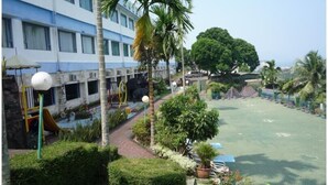 A courtyard with a playground, palm trees, and a building with multiple windows. - Hotel Marcopolo (Bandar Lampung)