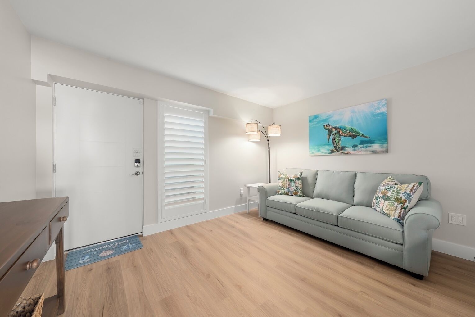 Uma sala de estar com um sofá cinzento, um quadro de uma tartaruga marinha e piso de madeira.