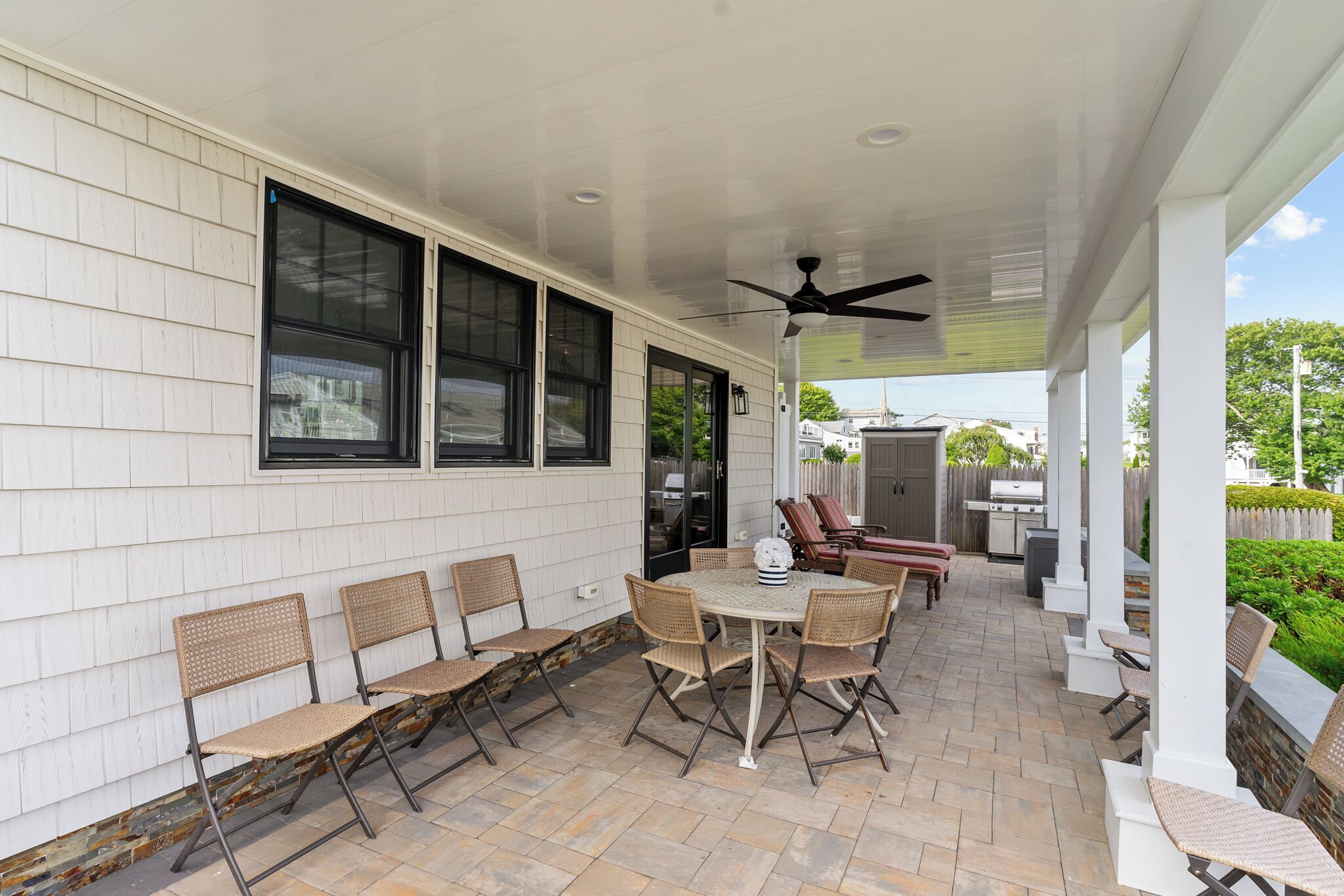 A covered patio with a table and chairs, a ceiling fan, and a grill area.