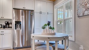 Una cocina moderna con muebles blancos, un refrigerador de acero inoxidable y una zona de comedor con una mesa redonda y sillas.