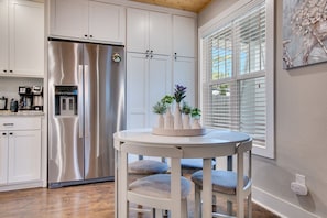A modern kitchen with white cabinetry, a stainless steel refrigerator, and a dining area with a round table and chairs. - Steps to Trails - Bentonville Home Near Square & Museums (Bentonville)