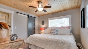 Un dormitorio con cama, cabecera de madera, ventilador de techo y ventana con persianas.