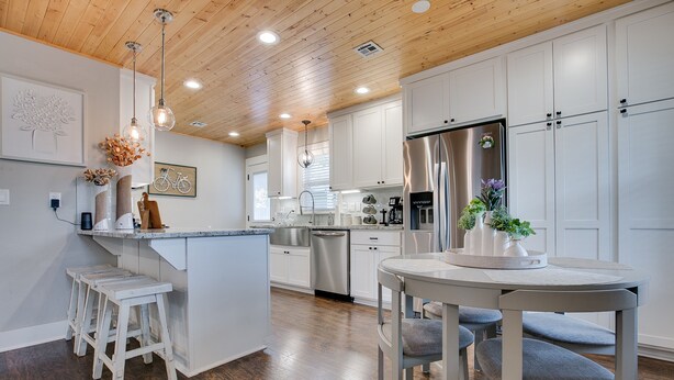 Una cocina moderna con armarios blancos, un refrigerador de acero inoxidable y techo de madera.