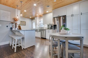 Una cocina moderna con armarios blancos, un refrigerador de acero inoxidable y techo de madera.