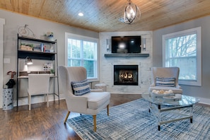 A living room with a fireplace, two armchairs, a coffee table, and a bookshelf. - Steps to Trails - Bentonville Home Near Square & Museums (Bentonville)