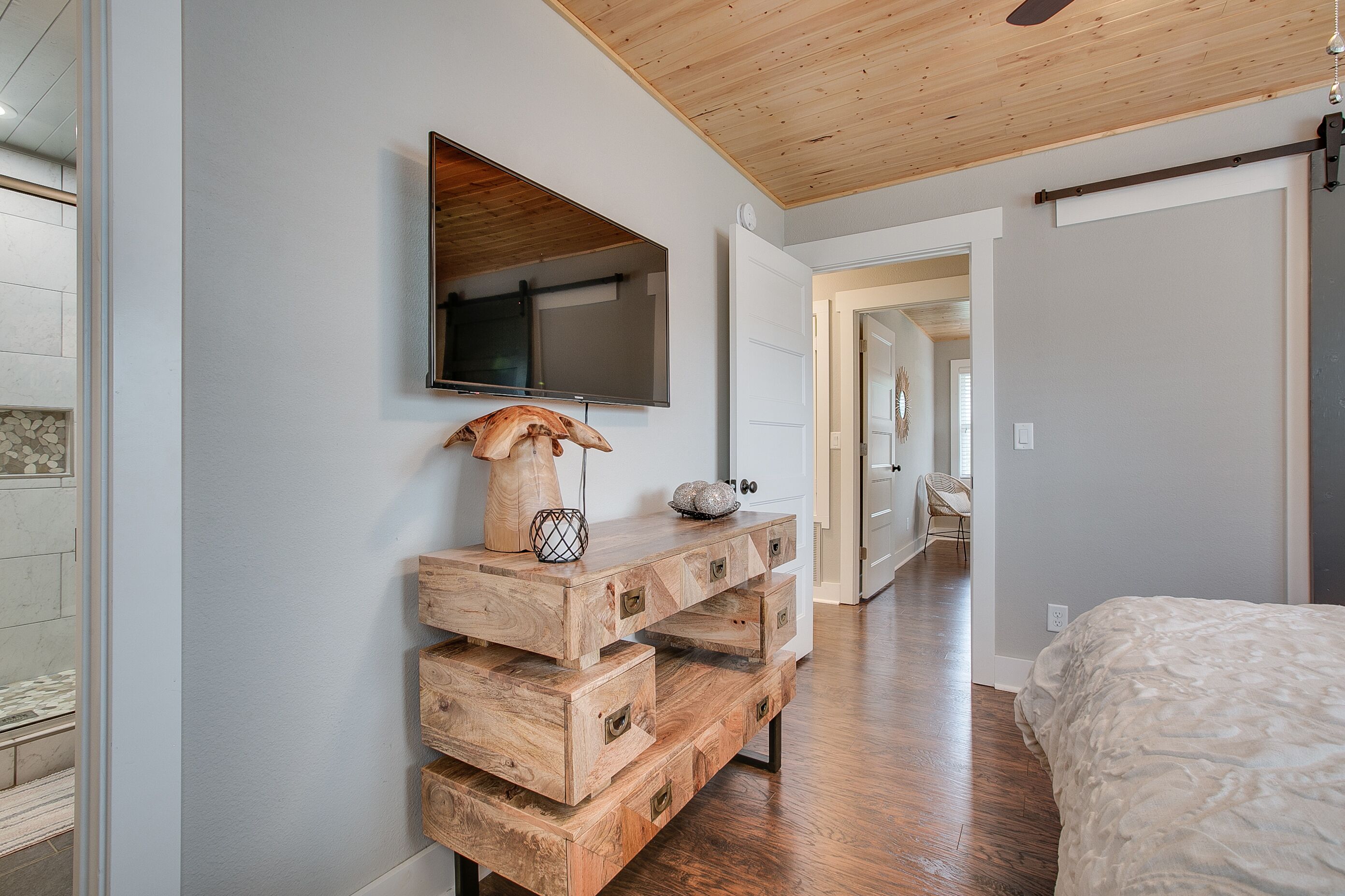 Un dormitorio moderno con una mesa consola de madera, un televisor de pantalla plana y una cama con cubrecama texturizado.