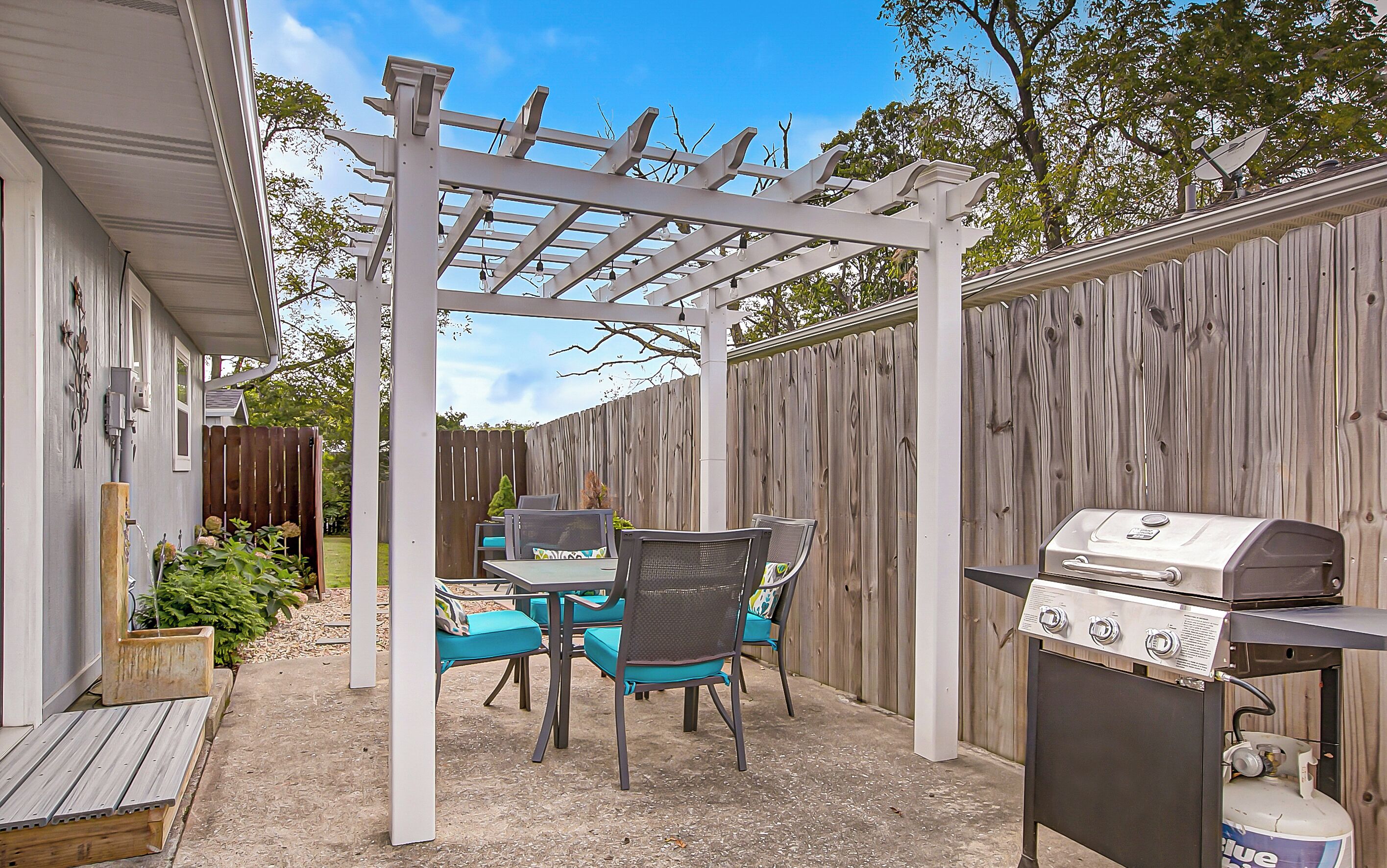 An outdoor patio with a pergola, a grill, and a table with chairs.