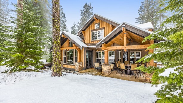 A log cabin with a stone foundation, large windows, and a covered outdoor seating area.