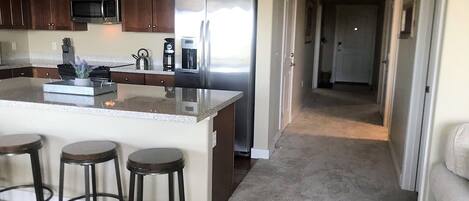 A kitchen with dark wooden cabinets, a stainless steel refrigerator, a microwave, and a coffee maker. There are three stools at the kitchen island.