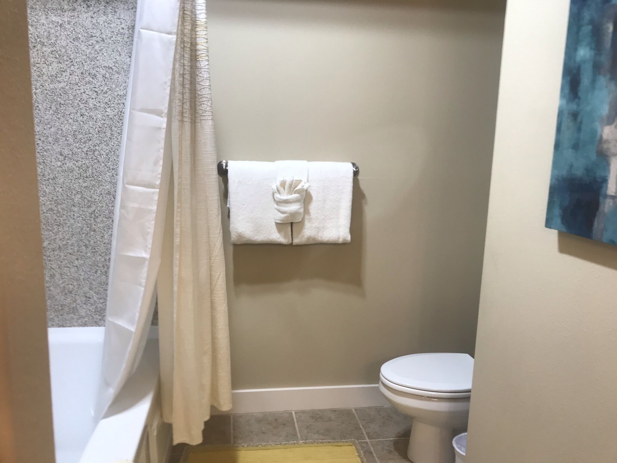 Un baño con inodoro, una toalla colgada en un perchero y cortina de ducha.