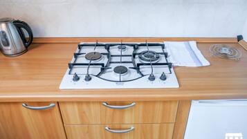 Une cuisine équipée d’une cuisinière à gaz, d’une bouilloire et d’un égouttoir à vaisselle.