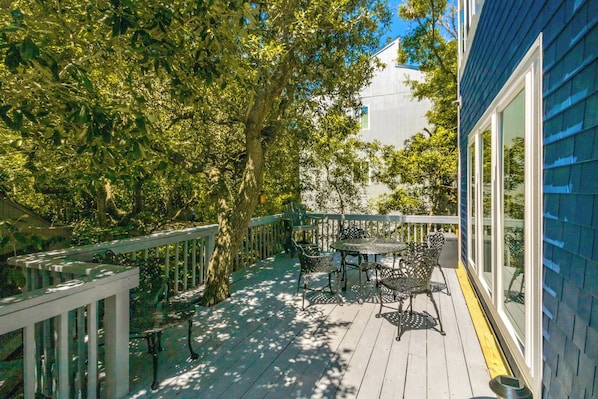 A wooden deck with a table and chairs, surrounded by trees and a building. - Always Beachin' - Custom Home in quiet Channelbend; Sleeps 10 (Surf City)