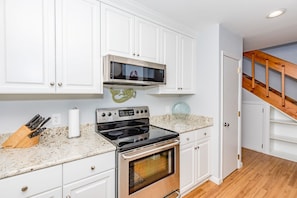A kitchen with white cabinets, a stainless steel stove, a microwave, and a wooden staircase. - Always Beachin' - Custom Home in quiet Channelbend; Sleeps 10 (Surf City)