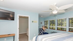 A bedroom with a bed, a ceiling fan, a TV mounted on the wall, and a window with blinds.
