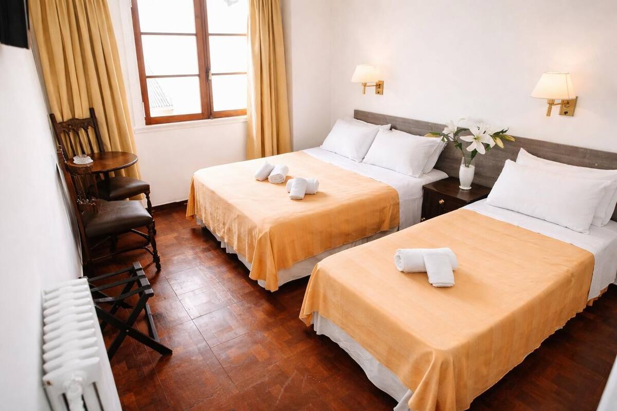 Une chambre d’hôtel avec deux lits, un bureau, une chaise, une fenêtre avec des rideaux et des lampes fixées au mur.