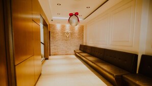 Een hal met een bruine leren bank, een structuurwand en een plafond met inbouwverlichting en een decoratieve bol.