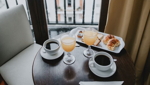 Een ronde houten tafel met een wit bord, een glas sinaasappelsap, een kop koffie en een croissant.