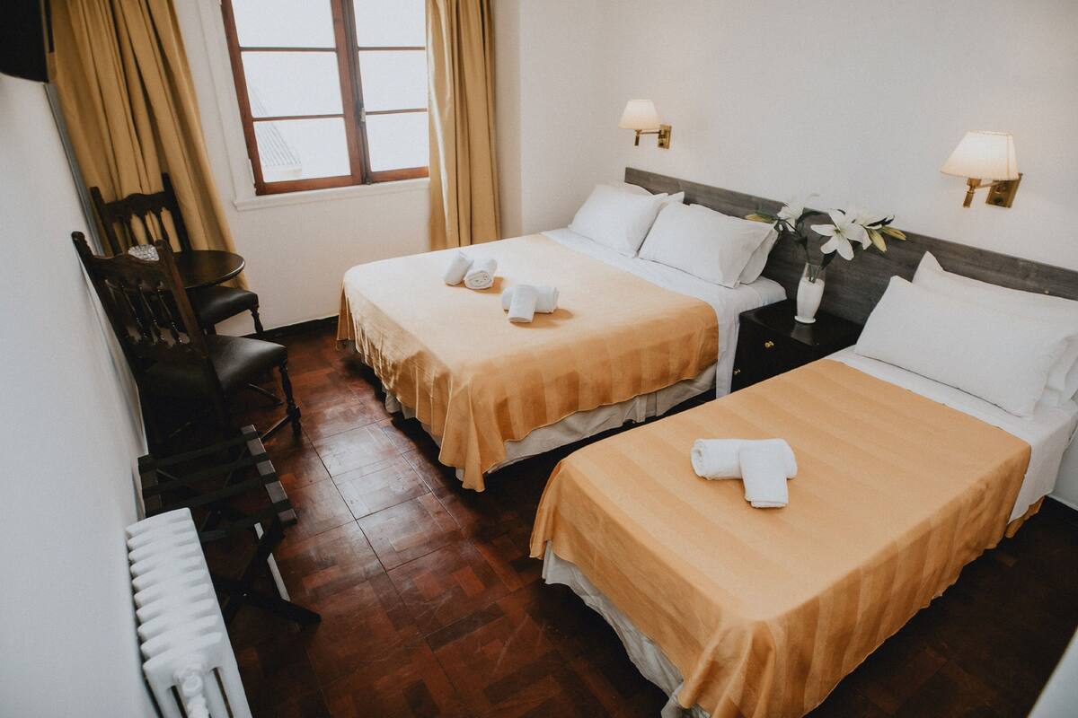 Une chambre d’hôtel avec deux lits, une chaise, une petite table et un radiateur.