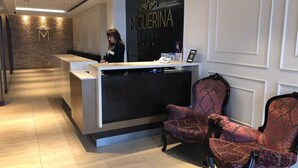 Een hotel receptie met een modern receptiebalie, twee gestreepten fauteuils, en een wandbordje met 'MIGLIERINA HOTEL'.
