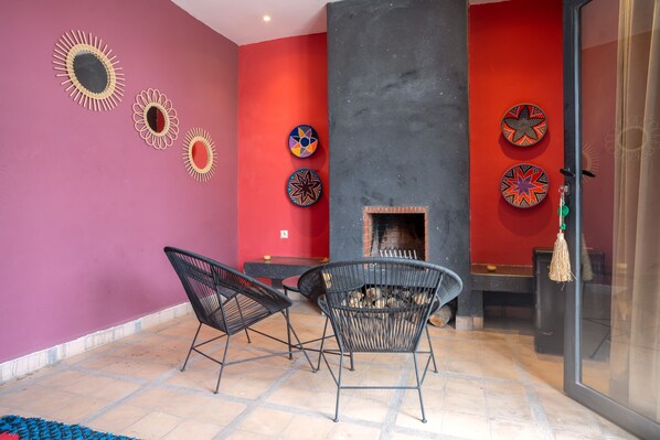 Une pièce avec une cheminée, deux fauteuils noirs, une table et des assiettes décoratives accrochées au mur.