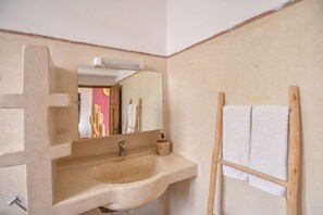 Casa de banho com pia bege, espelho e porta-toalhas de madeira.