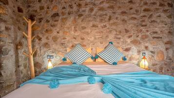 A bed in a stone-walled room with striped pillows and a blue blanket.