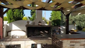 Un patio al aire libre con chimenea de piedra, banca de madera y una estructura de pérgola.