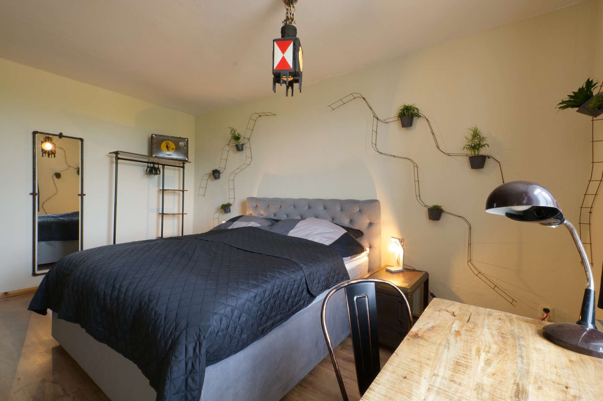 Ein Schlafzimmer mit Bett, Nachttisch, Lampe und Wandpflanzen.