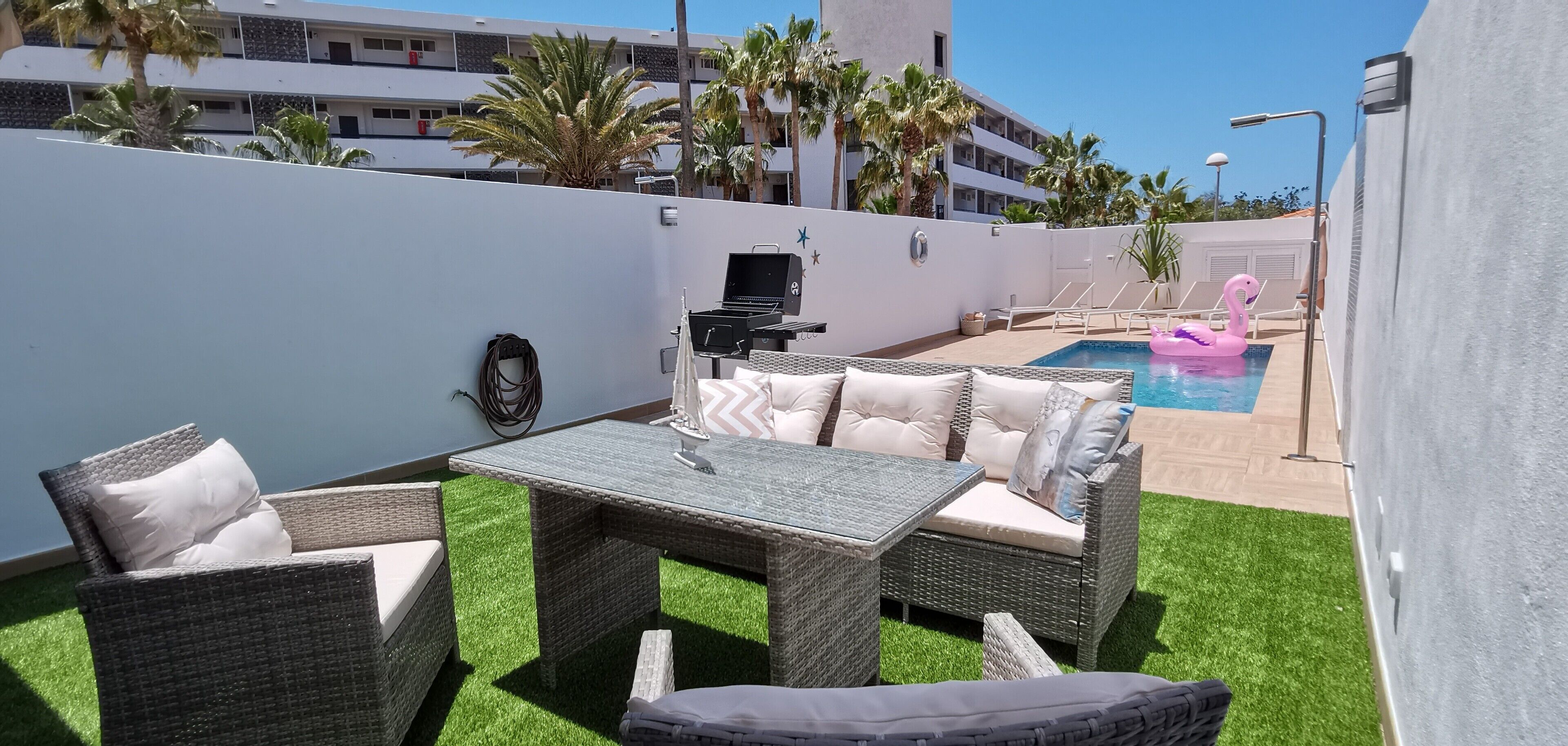 Une terrasse avec des meubles en osier, une piscine et des palmiers.