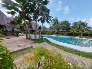 A swimming pool surrounded by palm trees and thatched-roof structures. - Sofia House (Malindi)
