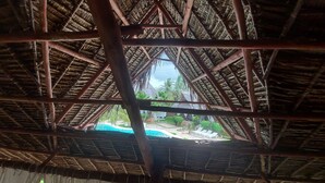 A thatched roof structure with visible wooden beams and a view of an outdoor swimming pool area. - Sofia House (Malindi)