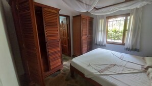 A bedroom with a bed, wooden wardrobe, and a window with curtains. - Sofia House (Malindi)