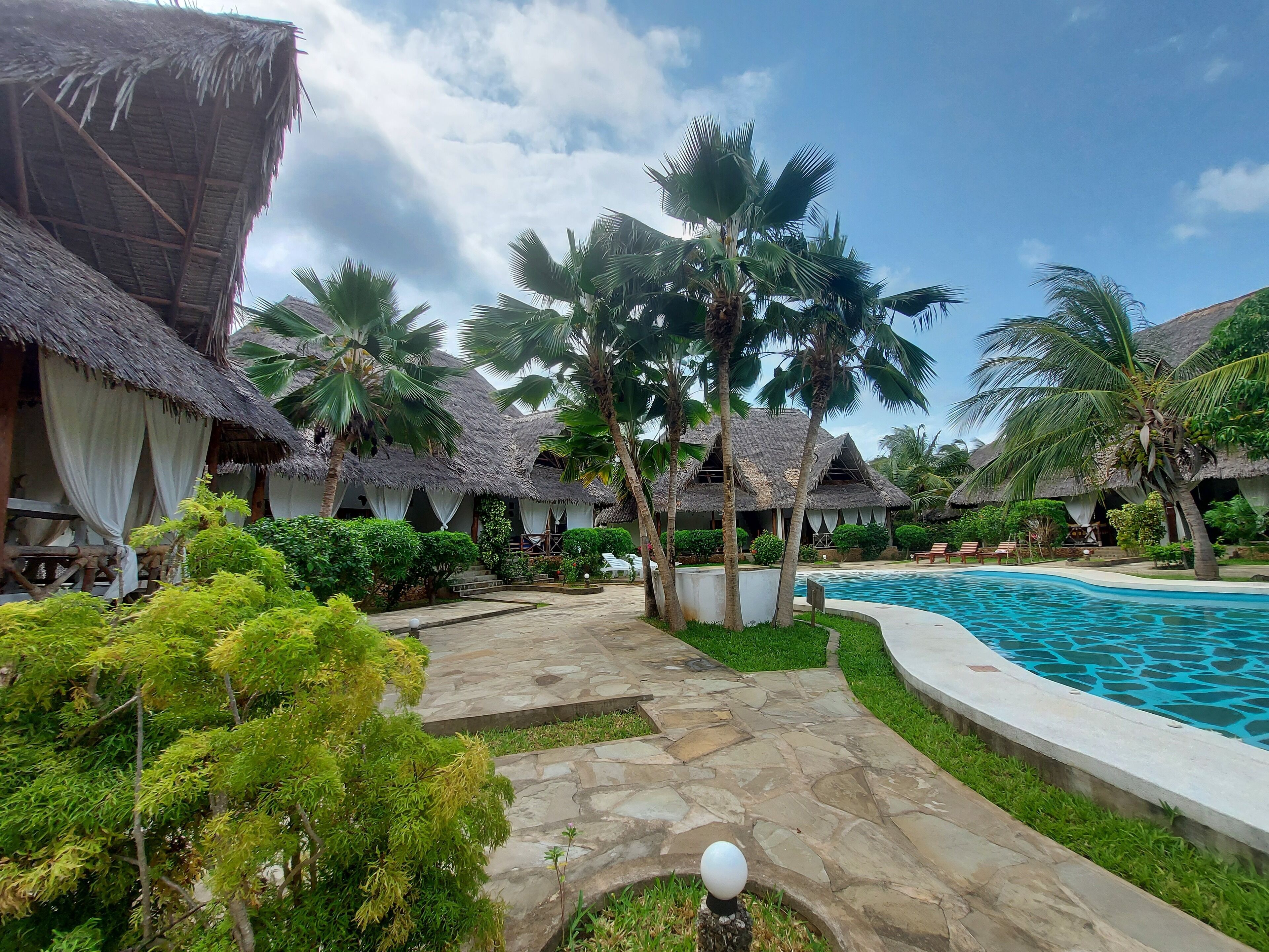 Un complexe hôtelier doté de bungalows aux toits de chaume, d’une piscine et d’une végétation luxuriante.