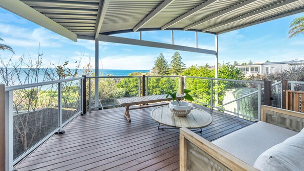 A wooden deck with a table and bench, overlooking a scenic view of the ocean and greenery. - RELAX @ Sea La Vie KIAMA Million Dollar Views (Kiama)