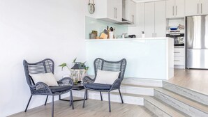 A modern kitchen with white cabinets, a stainless steel refrigerator, and a dining area with wicker chairs. - RELAX @ Sea La Vie KIAMA Million Dollar Views (Kiama)