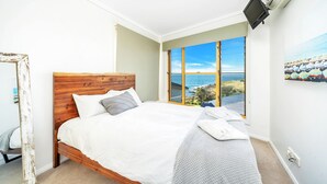 A bedroom with a wooden bed, a large window with a view of the sea, and a painting on the wall. - RELAX @ Sea La Vie KIAMA Million Dollar Views (Kiama)