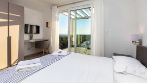 A modern hotel room with a bed, a desk, a TV, and a balcony with a glass door. - Villa Riviera (Sveti Lovrec Labinski)