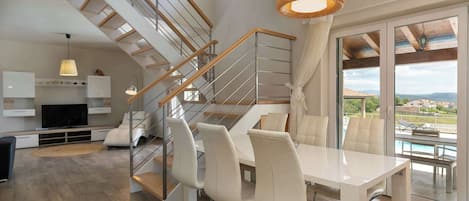 Un intérieur moderne avec un escalier, un coin repas et de grandes fenêtres.