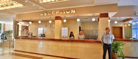 A reception area with a marble counter, a reception desk, and a potted plant.