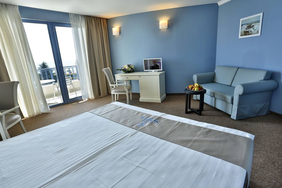 Une chambre d’hôtel avec un lit, un bureau avec un ordinateur, un canapé et une petite table avec des fruits.