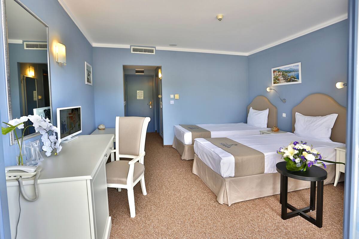 Une chambre d’hôtel avec deux lits, un bureau, une chaise, une petite table avec des fleurs et un miroir.