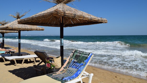 A beach with thatched umbrellas, lounge chairs, and a sign for Hotel Sofia Golden Sands. - Hotel Sofia - All Inclusive (Varna)