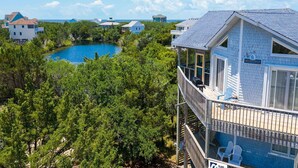 A beachfront property with a large pool surrounded by dense greenery, a multi-story building with a balcony, and a clear view of the ocean. - Soundside Dog Friendly w/ Hot Tub, Outdoor Games, Cmty Pool & Tennis/Pickleball (Avon)
