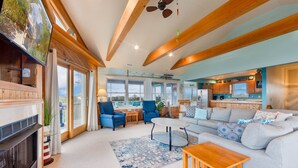 A spacious living area with a fireplace, a sofa, a coffee table, and a view of the outside. - Soundside Dog Friendly w/ Hot Tub, Outdoor Games, Cmty Pool & Tennis/Pickleball (Avon)