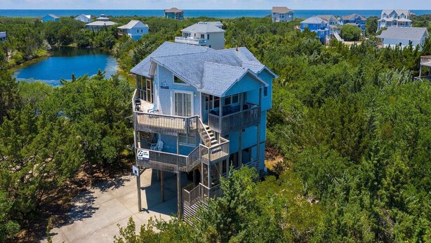 A multi-story house with a balcony, surrounded by dense greenery and a lake. - Soundside Dog Friendly w/ Hot Tub, Outdoor Games, Cmty Pool & Tennis/Pickleball (Avon)