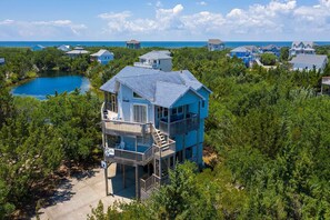 A multi-story house with a balcony, surrounded by dense greenery and a lake.