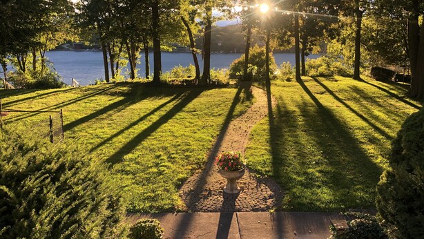 A well-maintained lawn with a paved path leading to a body of water, surrounded by trees and a bench.