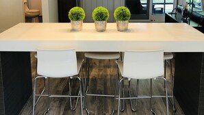A modern kitchen with a large island, three potted plants, and a unique light fixture.