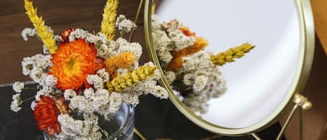 Un jarrón de vidrio con un ramo de flores y un pequeño espejo sobre una superficie oscura.